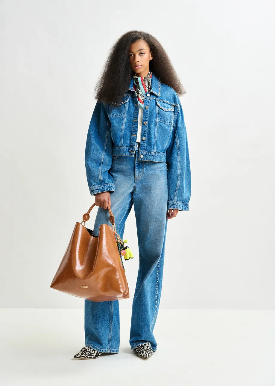 Person wearing a denim jacket and jeans holding a brown leather bag on a white background