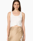 A model wearing a white ribbed knit tank top with a twisted front detail and a beige satin skirt with lace trim, set against a plain light gray background.