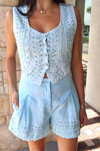 Woman wearing a light blue sleeveless top and shorts set with a textured wall background