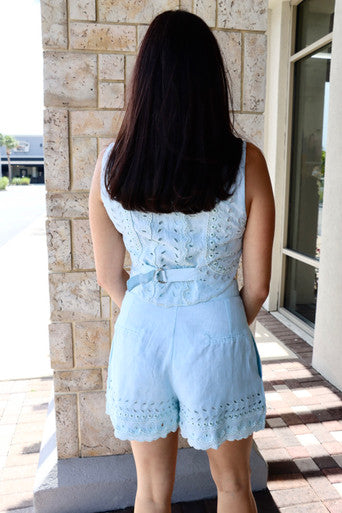 Woman wearing a light blue romper standing in front of a stone wall.