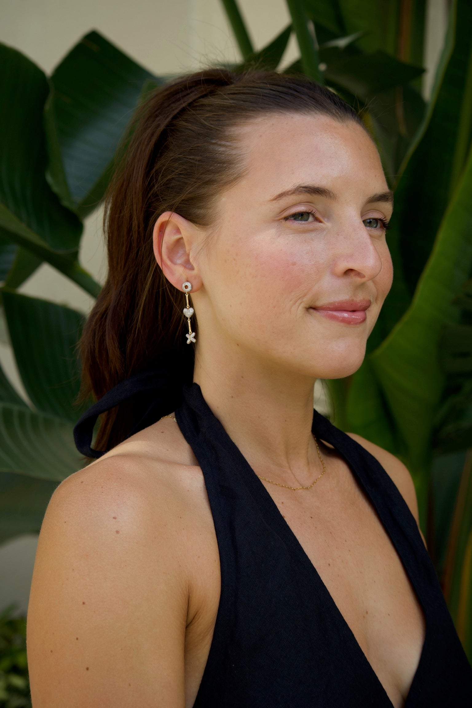 Woman wearing a black dress and xoxo earrings with plants in the background