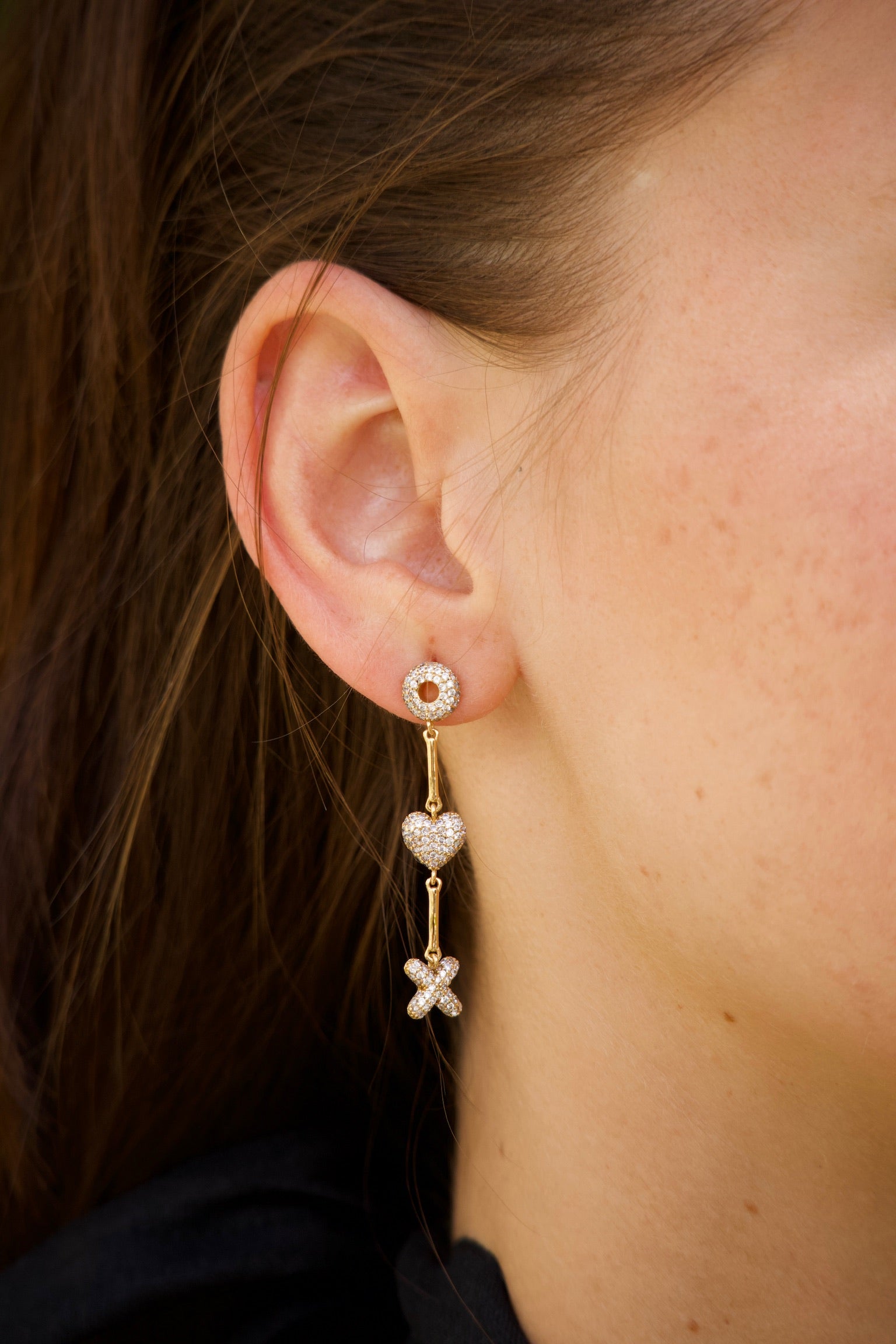Close-up of a person wearing gold earrings with heart and x and o designs.