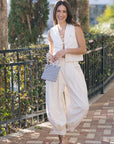 Woman in a white outfit with a patterned clutch walking outdoors.
