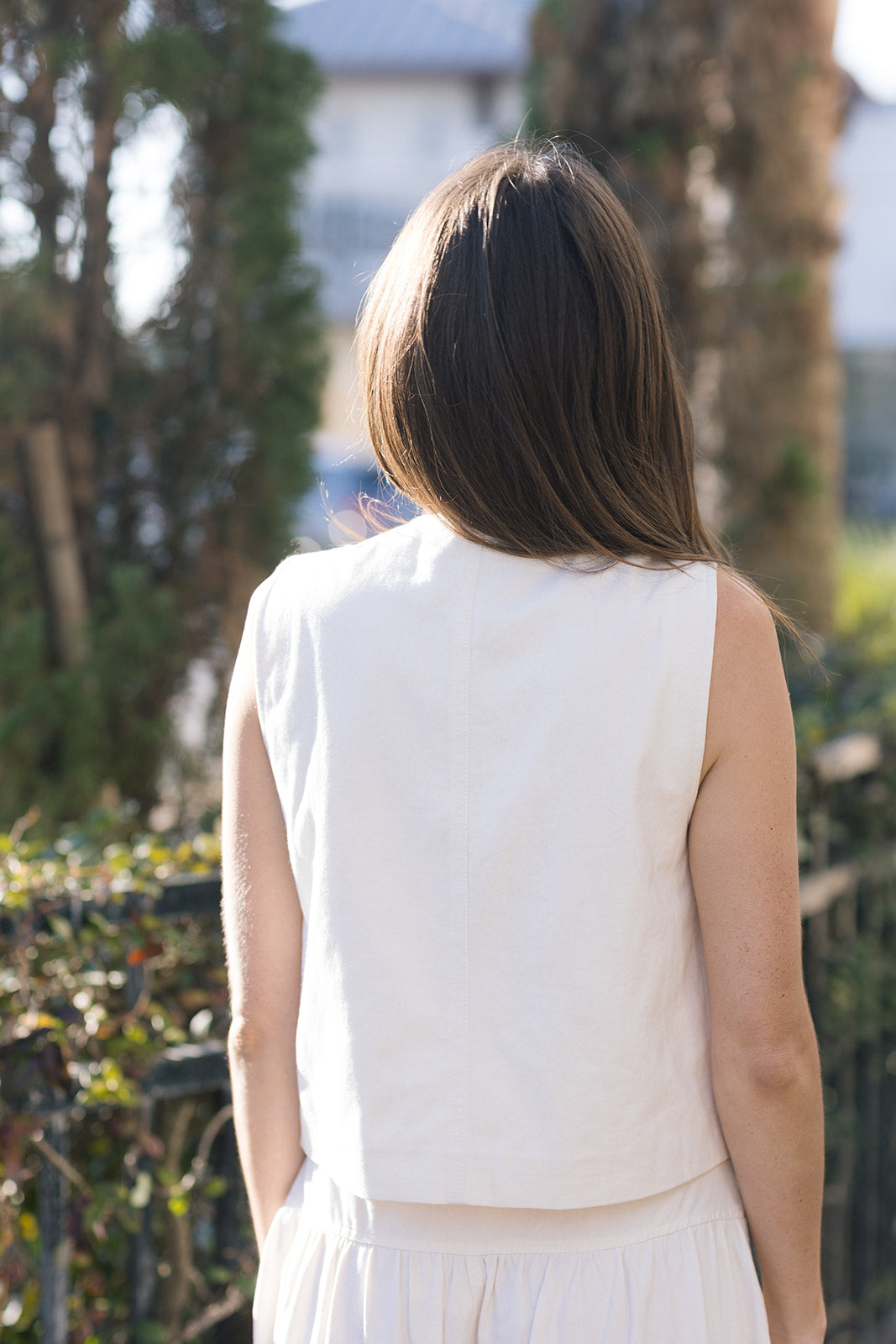 Person wearing a white sleeveless top outdoors with trees and buildings in the background