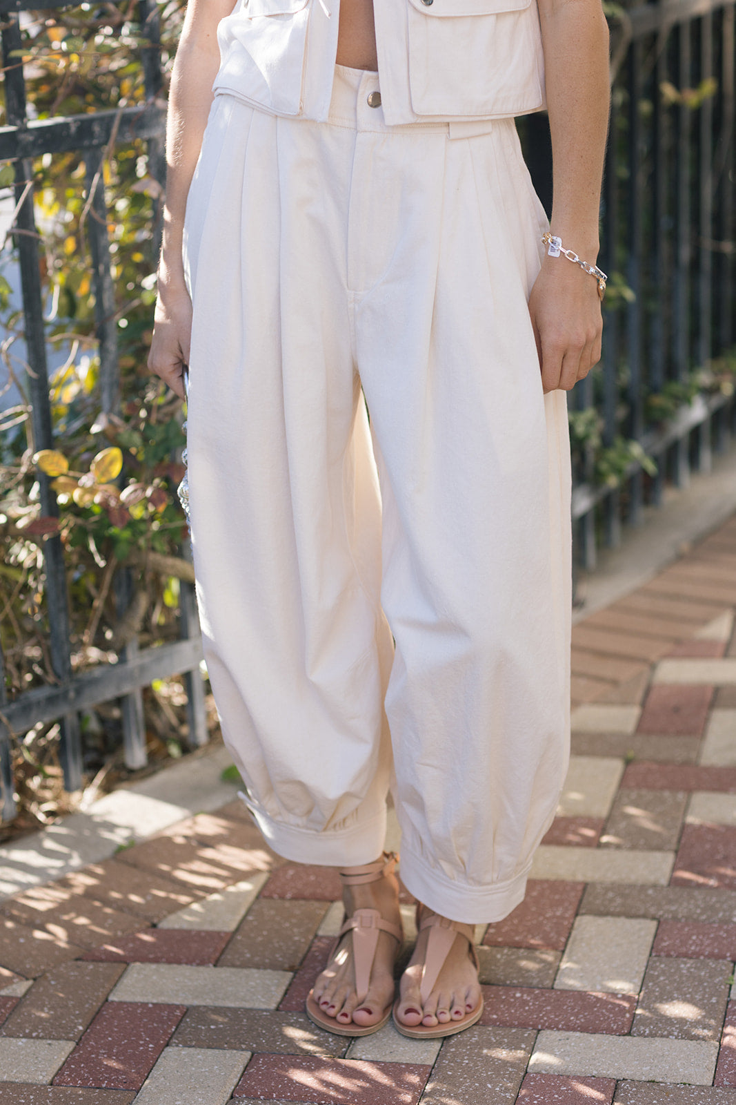 Person wearing white pants and sandals on a paved walkway with plants in the background