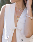 Close-up of a person wearing a white sleeveless top with buttons, a necklace, and a bracelet.