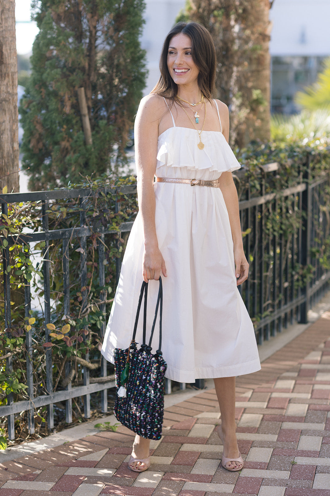 Woman in a white dress standing outdoors with greenery and a fence in the background