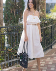 Woman in a white dress standing outdoors with greenery and a fence in the background