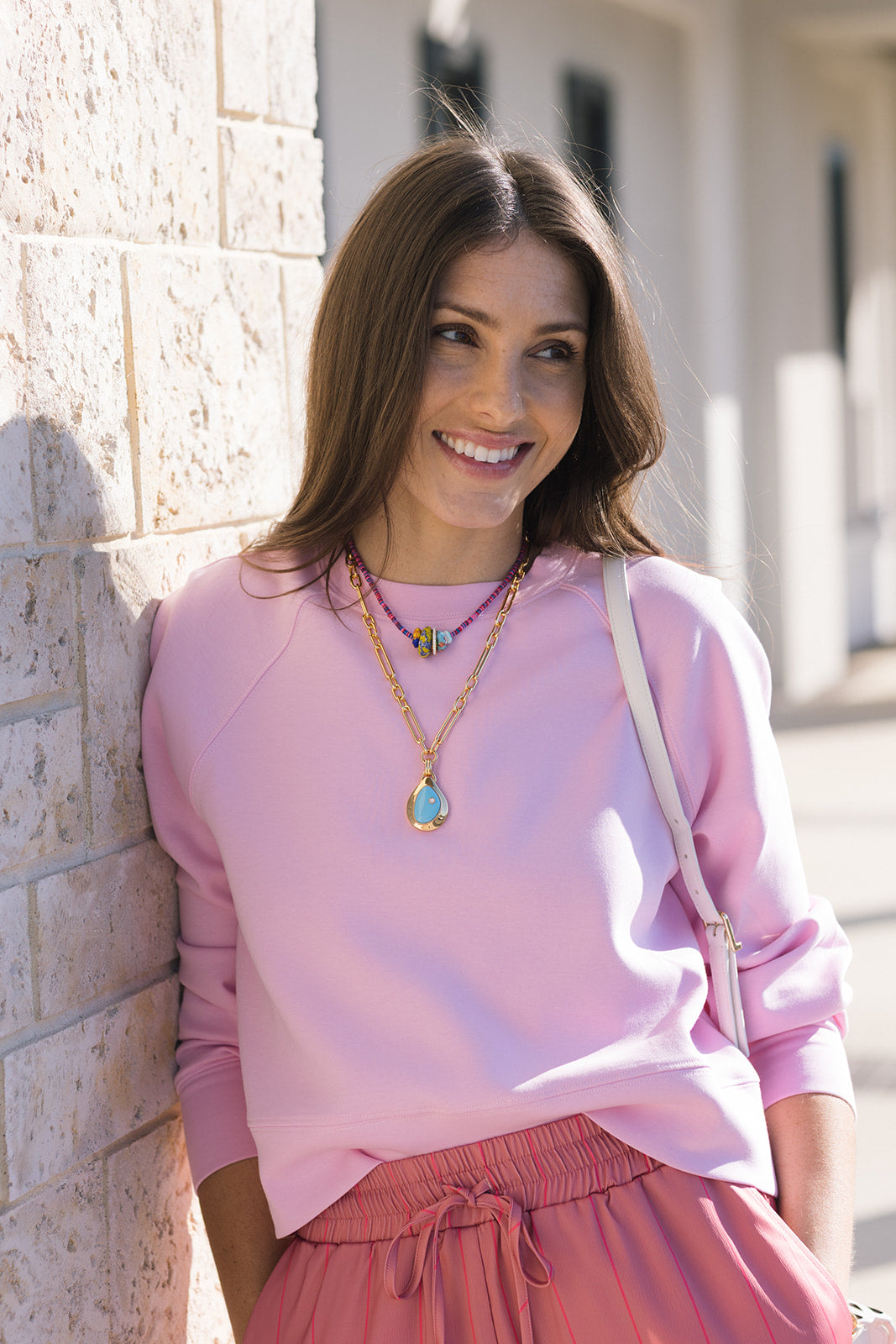 model wearing the nell sweatshirt in sugar pink leaning against a brick wall