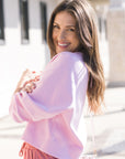 Woman wearing a pink sweater and pink pants standing outdoors.