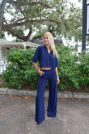 Woman in a blue outfit standing outdoors with greenery in the background, full body