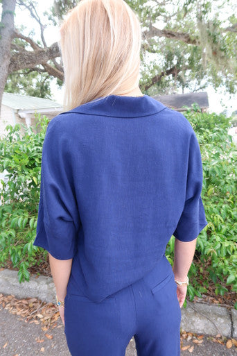Person wearing a blue suit standing outdoors with greenery in the background, back view