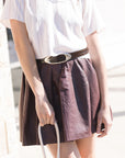 Person wearing a white shirt and brown skirt with a belt, holding a white bag.