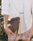 Person wearing a white blazer and lace shorts, holding a patterned clutch.