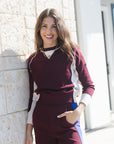 model wearing a burgundy sweater with white details and burgundy pants with a blue stripe leaning against a brick wall 