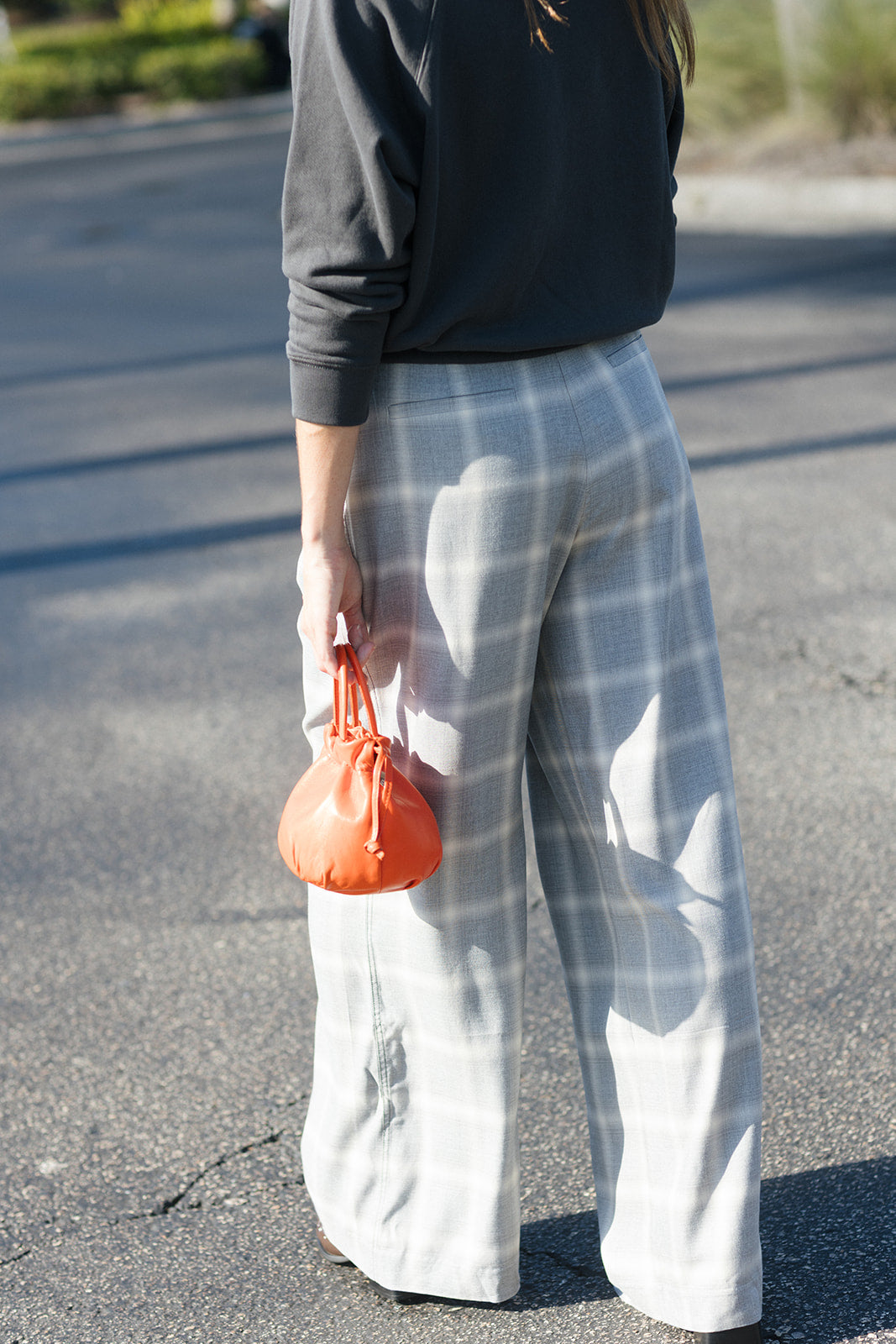 back view of a model wearing a sweatshirt and an orange bag in a parking lot