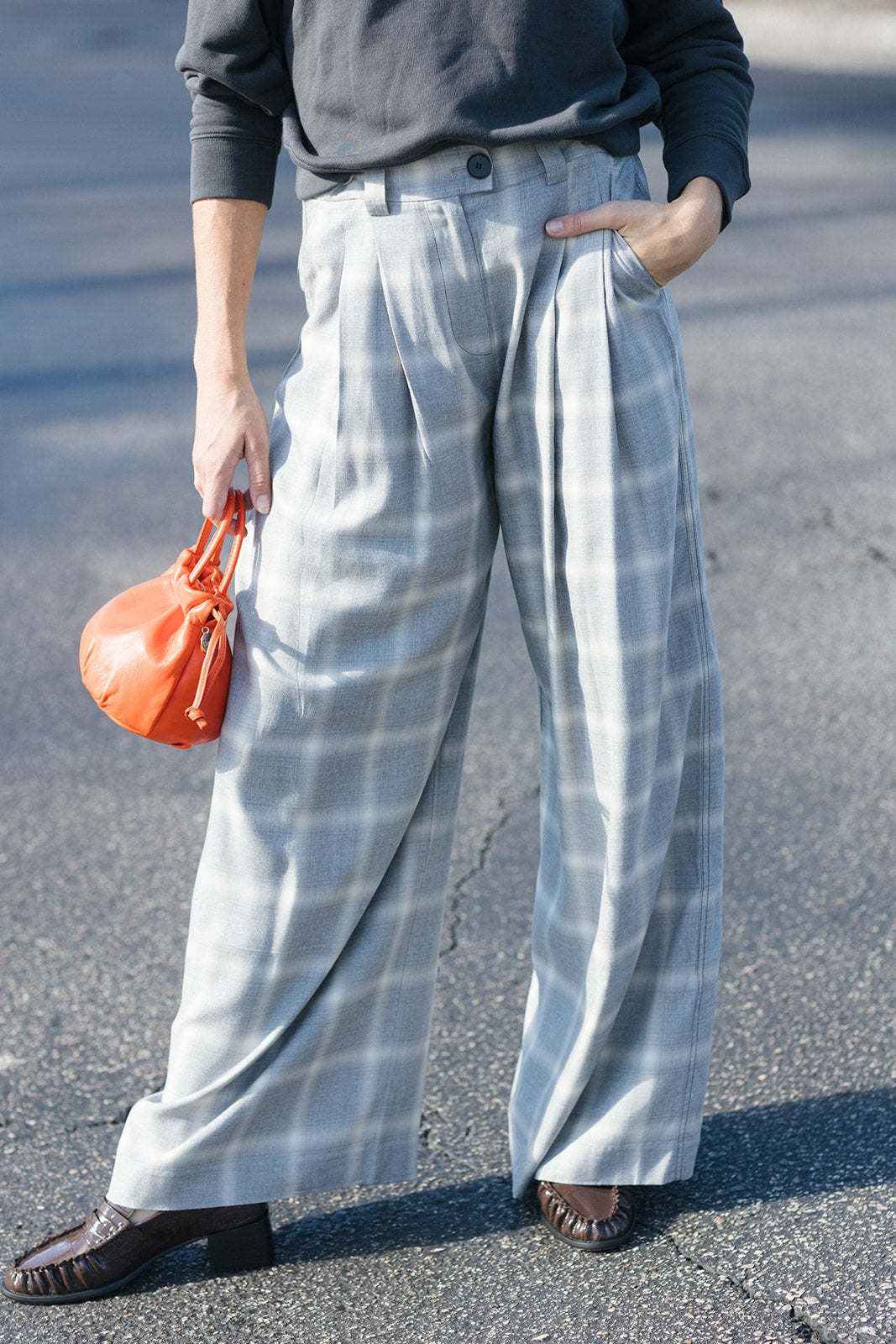 model wearing plaid pant with an orange bag and a sweatshirt in a parking lot