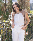 Woman wearing a white outfit with a brown sweater over her shoulders in an outdoor setting