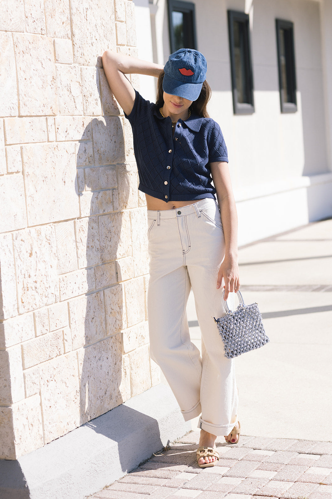 Person wearing a navy shirt, white pants, and a blue cap, standing against a light-colored wall.