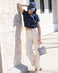 Person wearing a navy shirt, white pants, and a blue cap, standing against a light-colored wall.