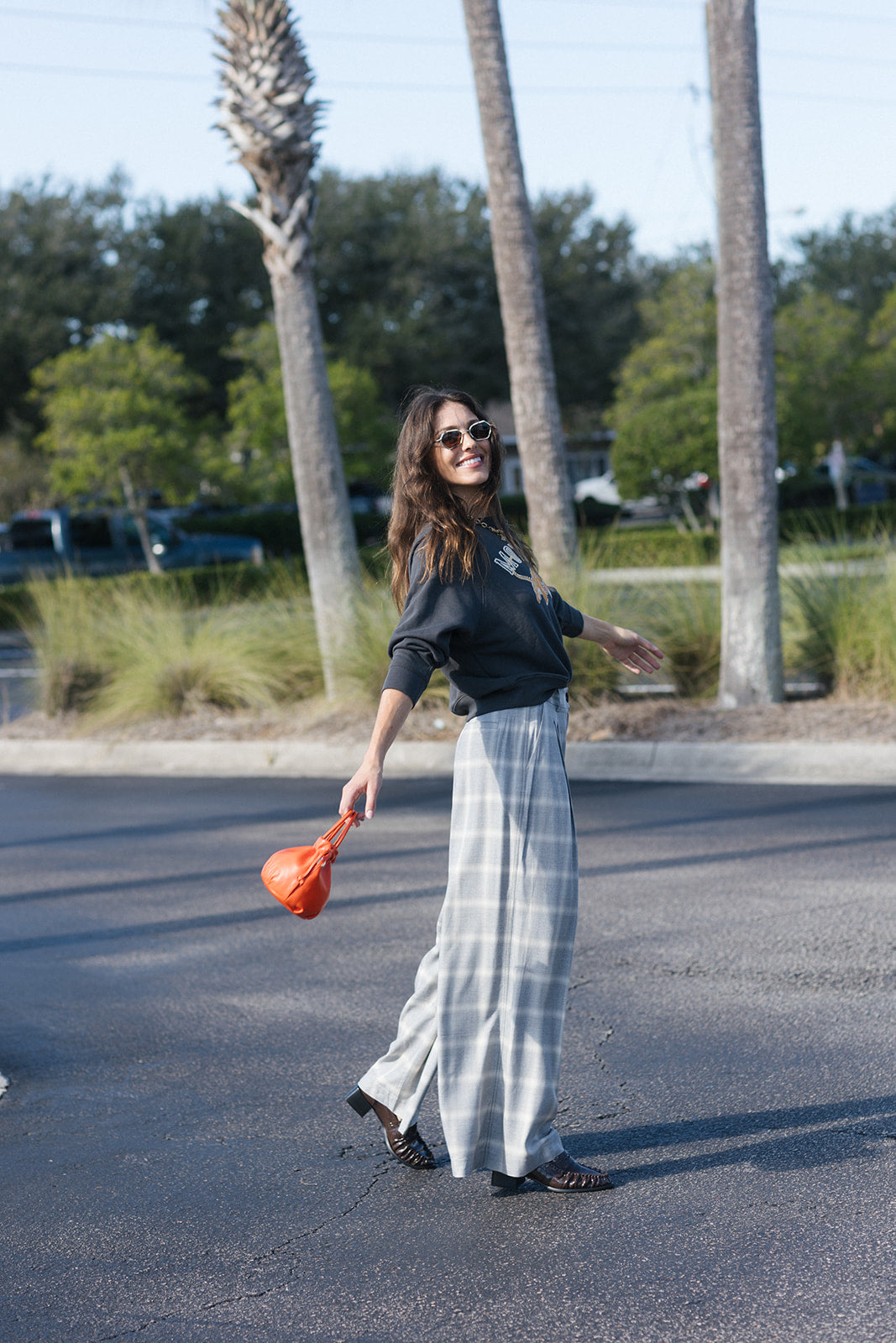 model wearing plaid pant with an orange bag and a sweatshirt in a parking lot