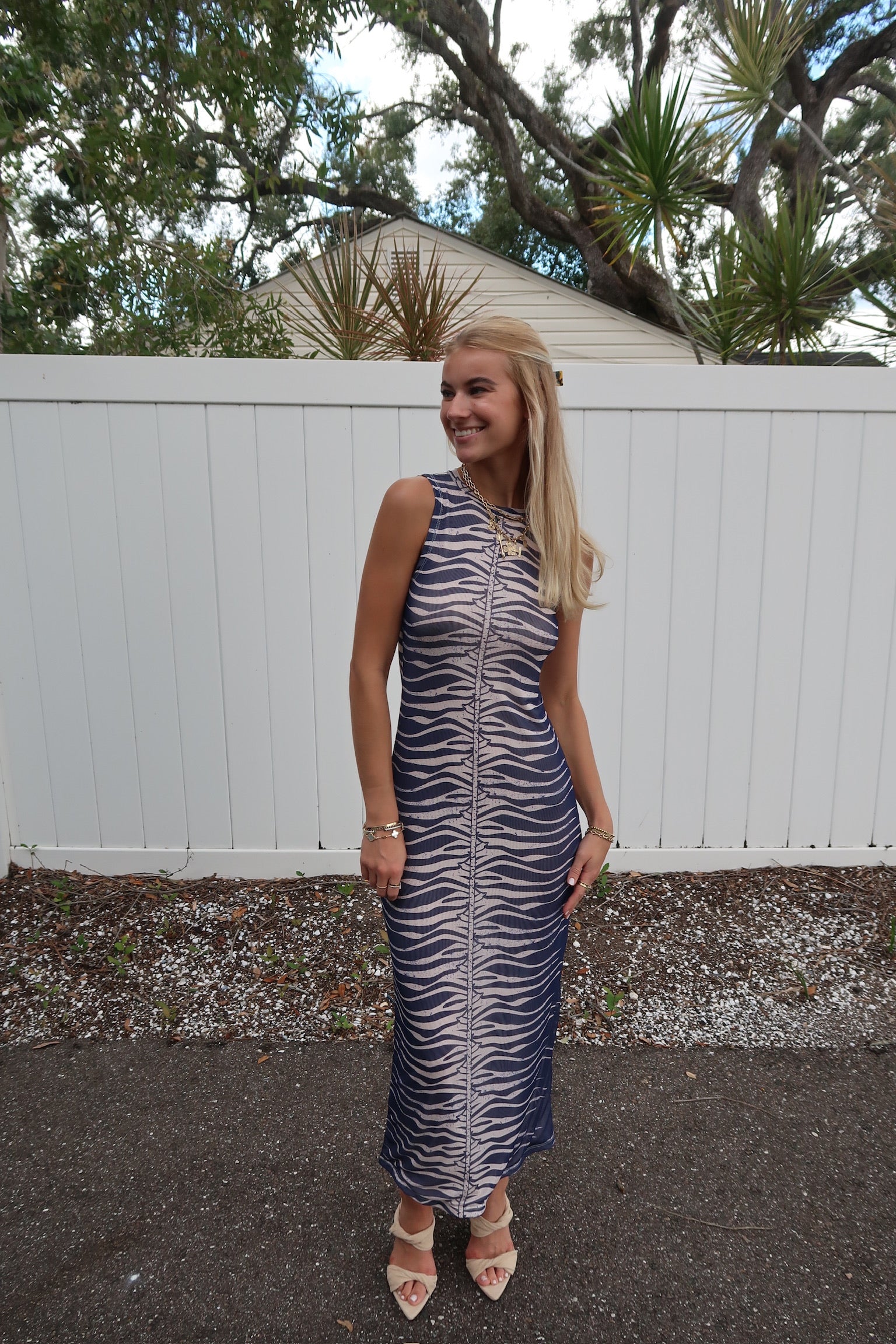 Woman in a zebra-striped dress standing outdoors with a white fence and trees in the background.