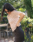 A woman wearing a light pink short-sleeve blouse with black polka dots and a dark brown mini skirt, standing outdoors in a garden setting.