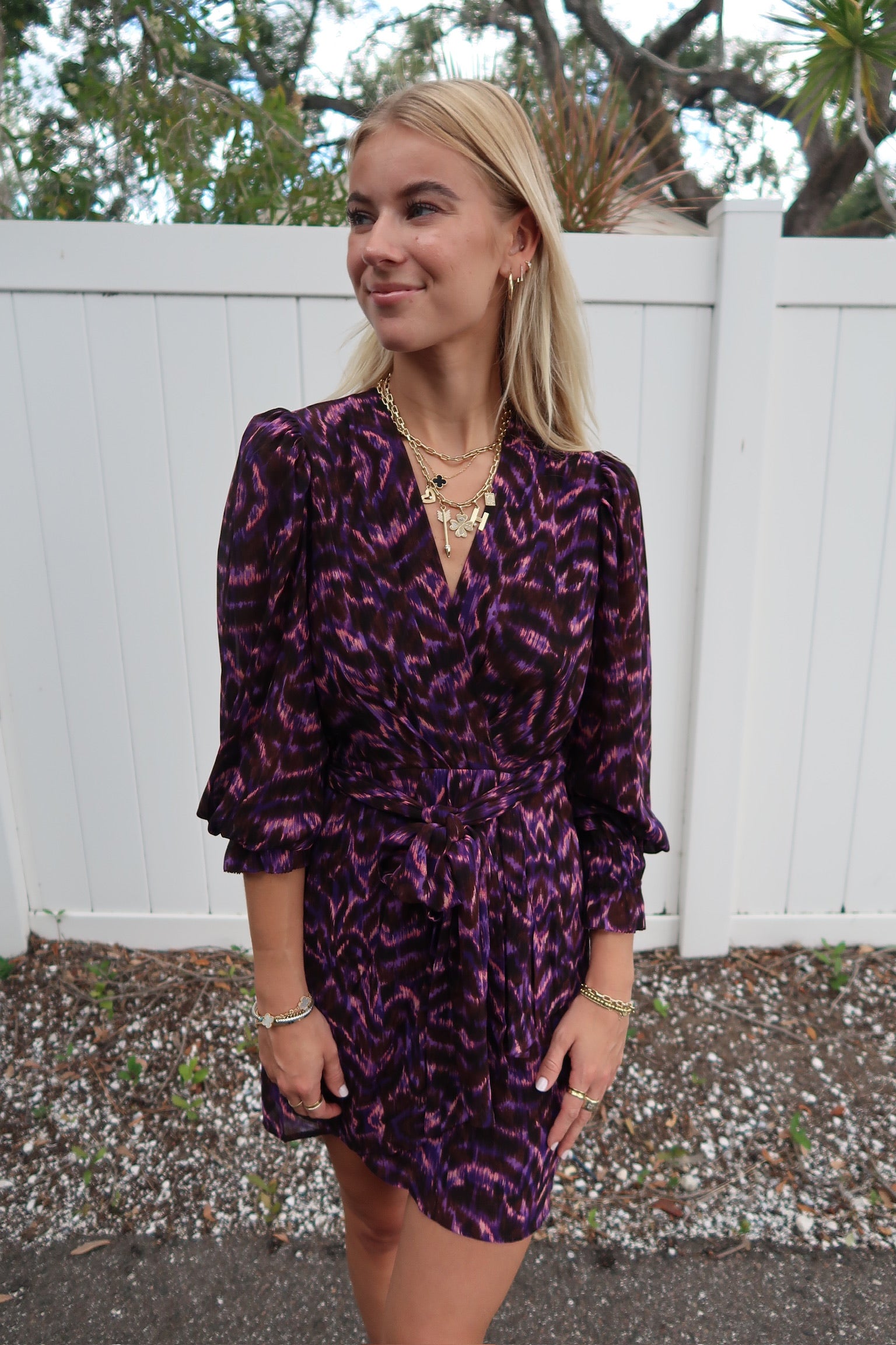Woman wearing a purple patterned dress standing in front of a white fence, close up front