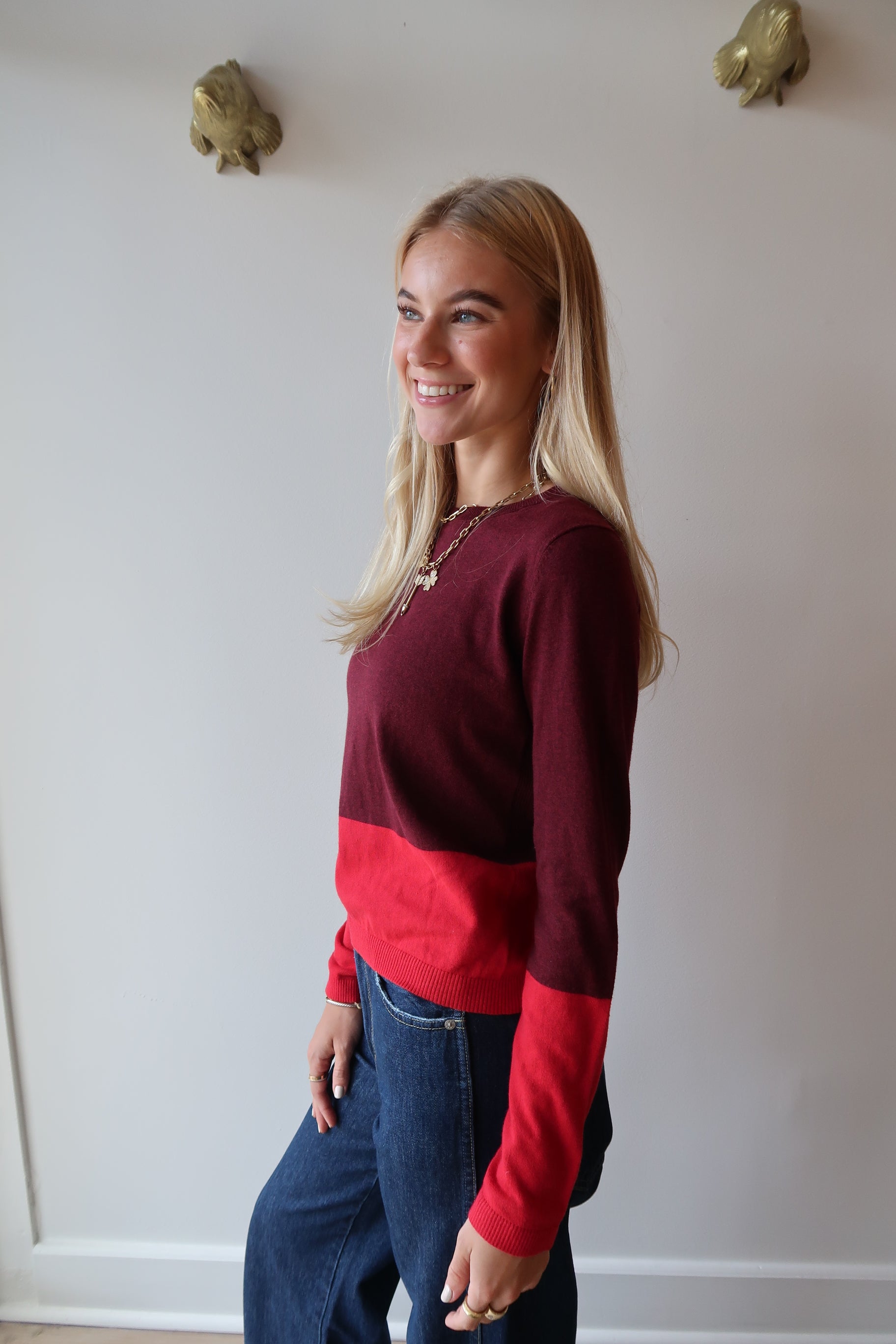 Woman wearing a red and maroon sweater standing against a white wall, side view