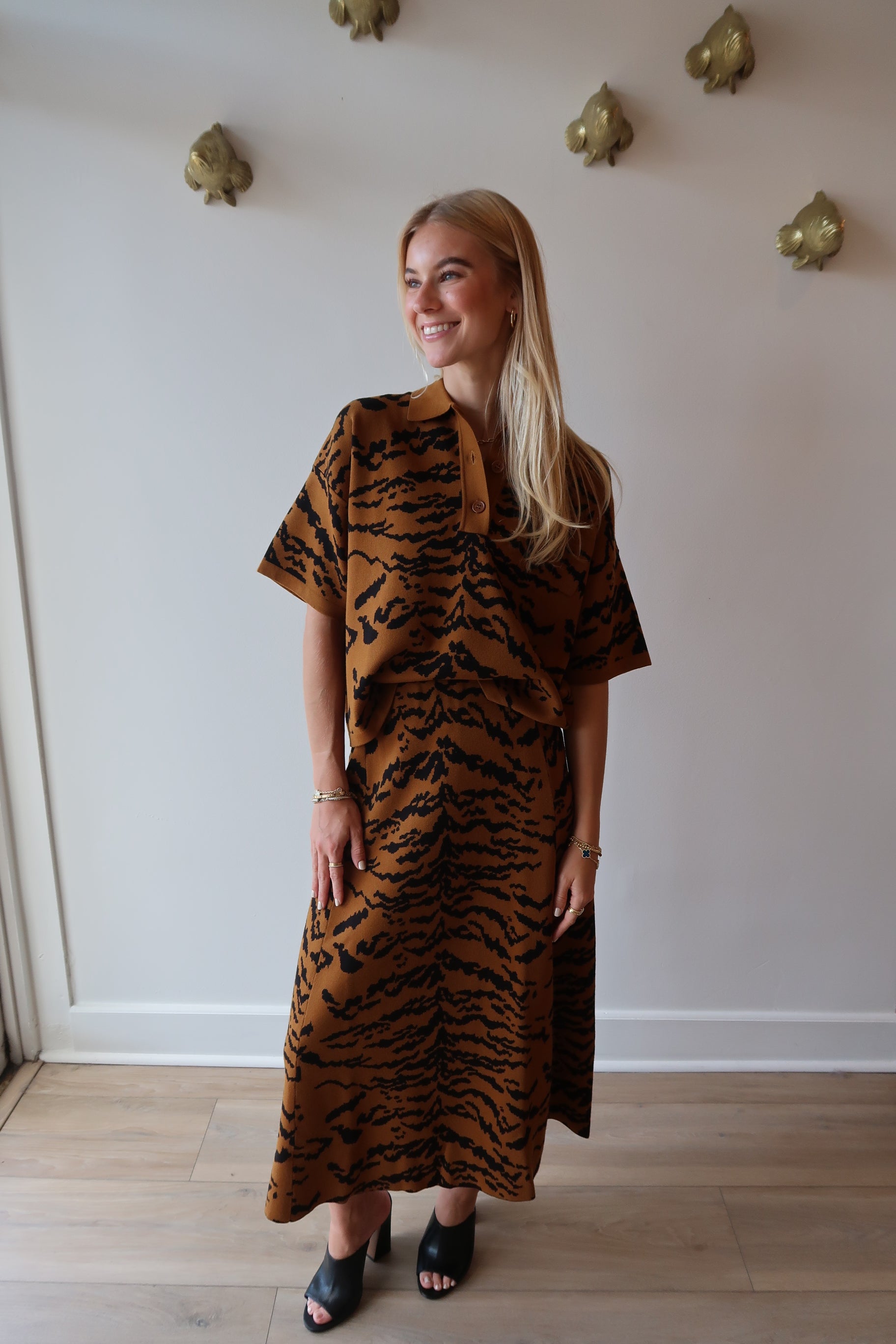 Woman wearing a tiger print set standing in a room with white walls and wooden flooring.