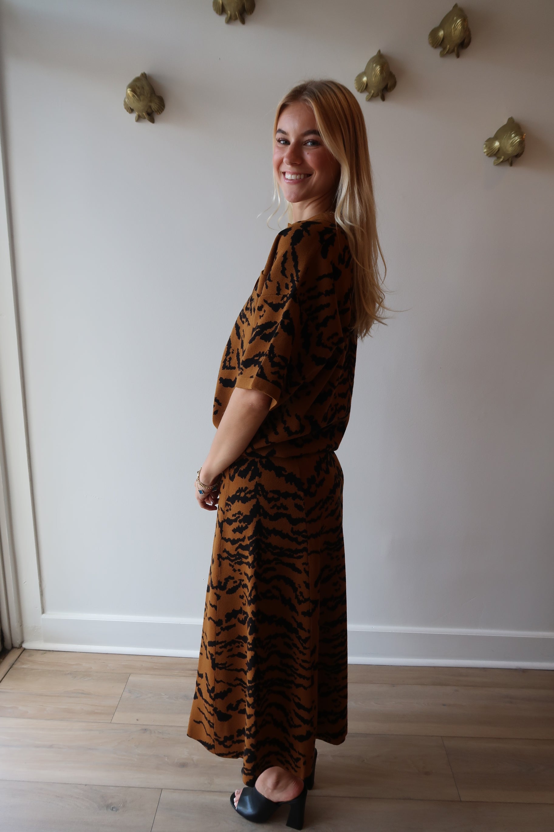 Person wearing a tiger print outfit standing in a room with white walls and wooden flooring, side view