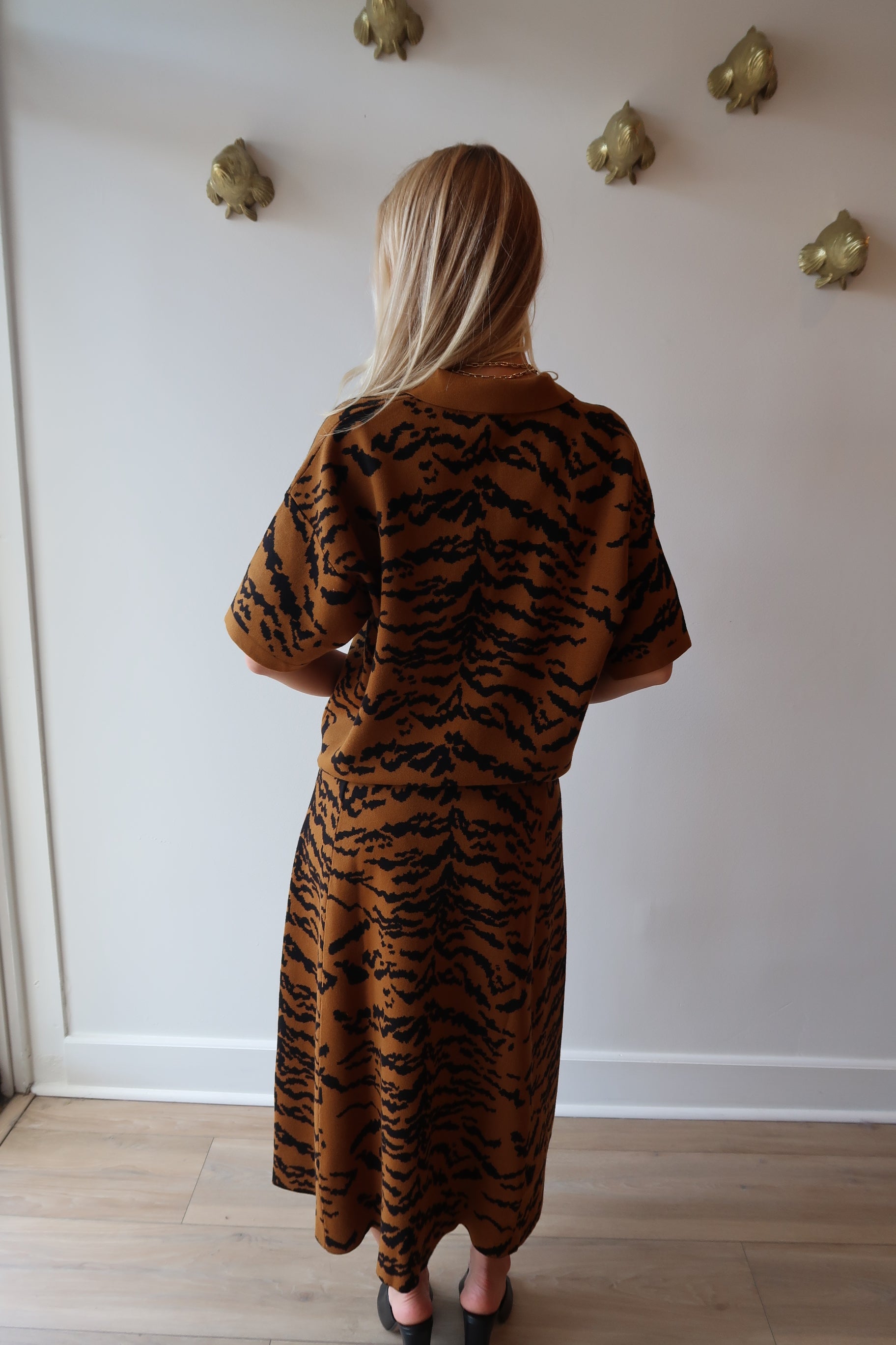 Person wearing a tiger-striped outfit standing against a white wall, back
