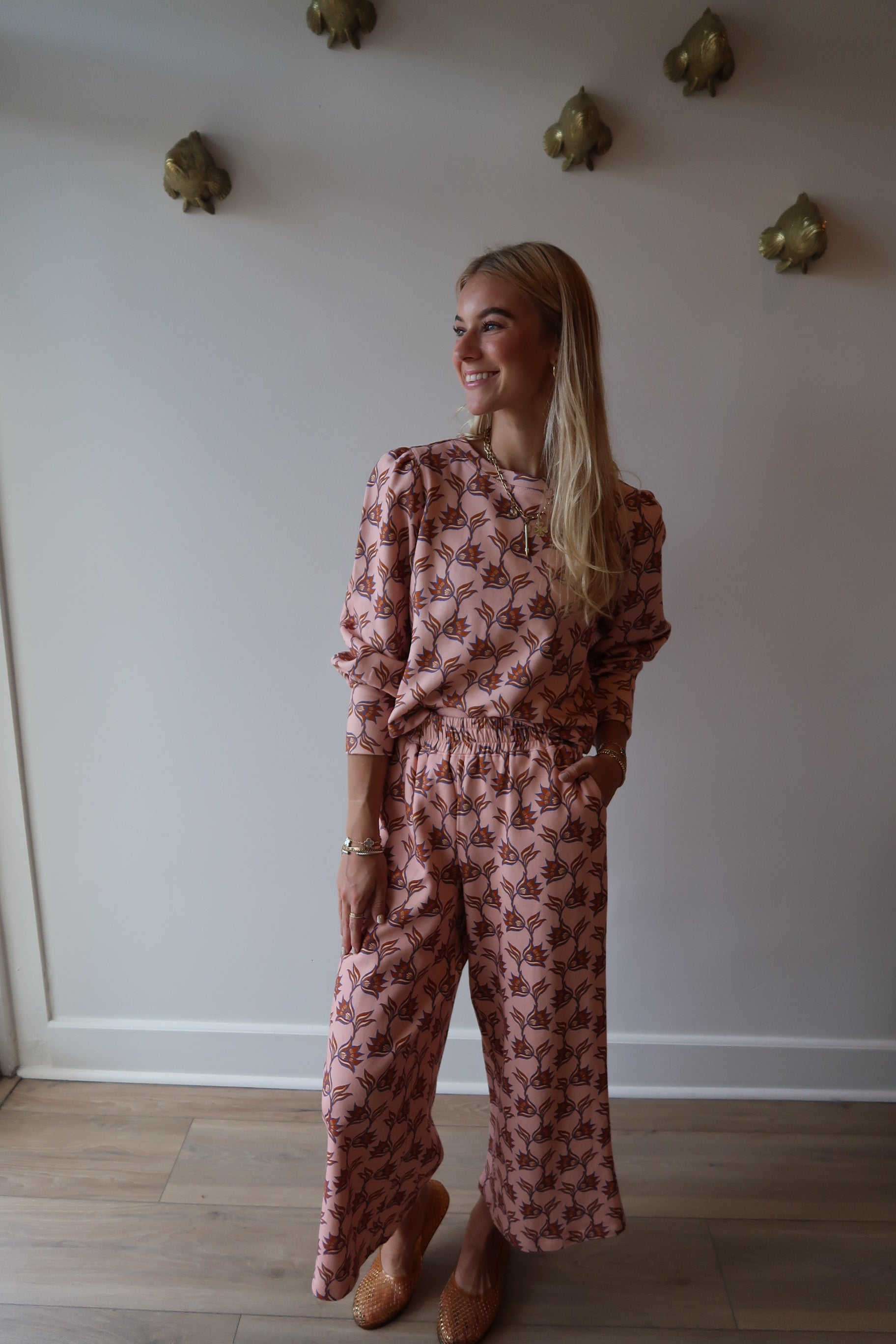 Person wearing a pink floral outfit standing in a room with white walls and wooden flooring.