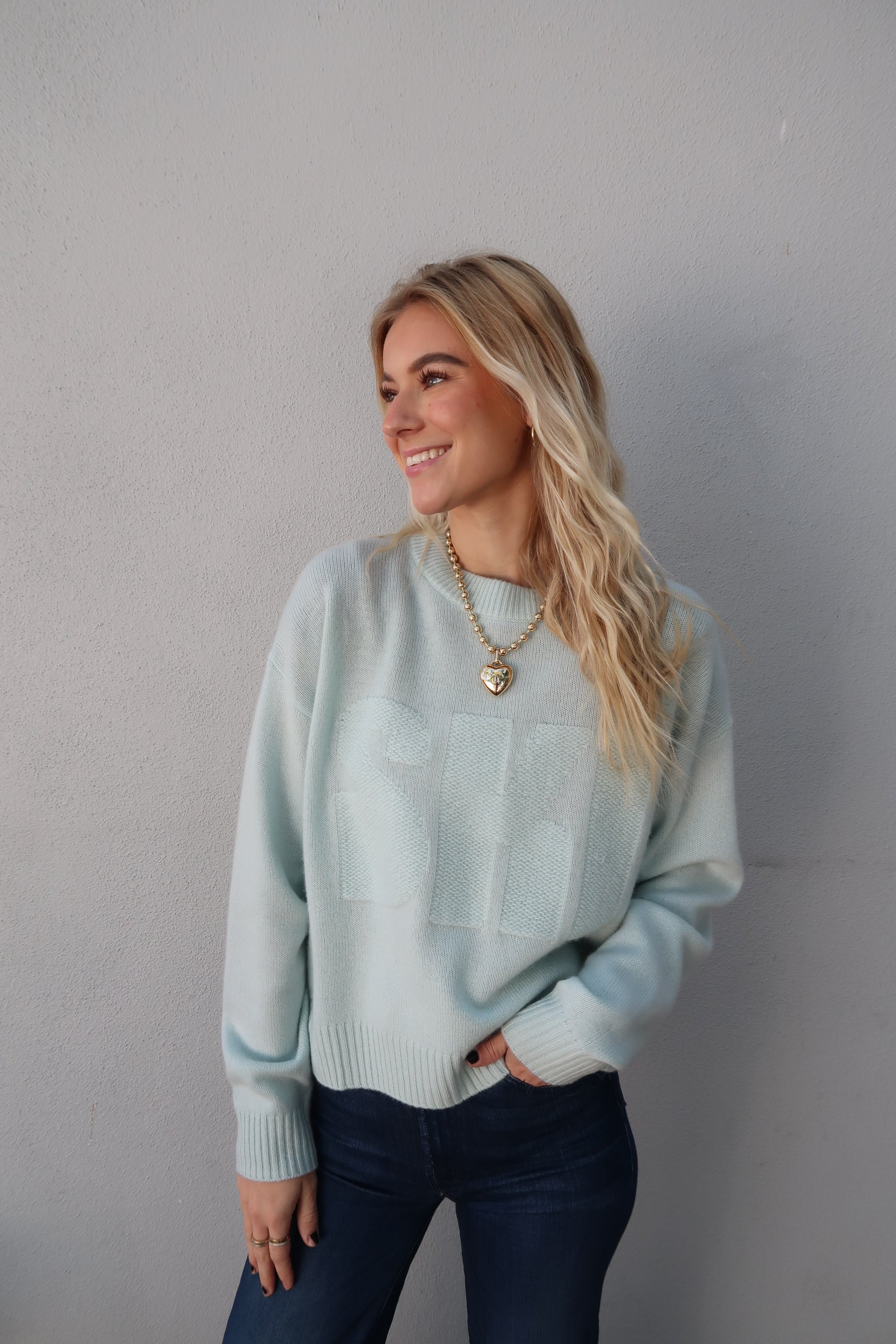 Woman wearing a light blue sweater and dark jeans on a plain background