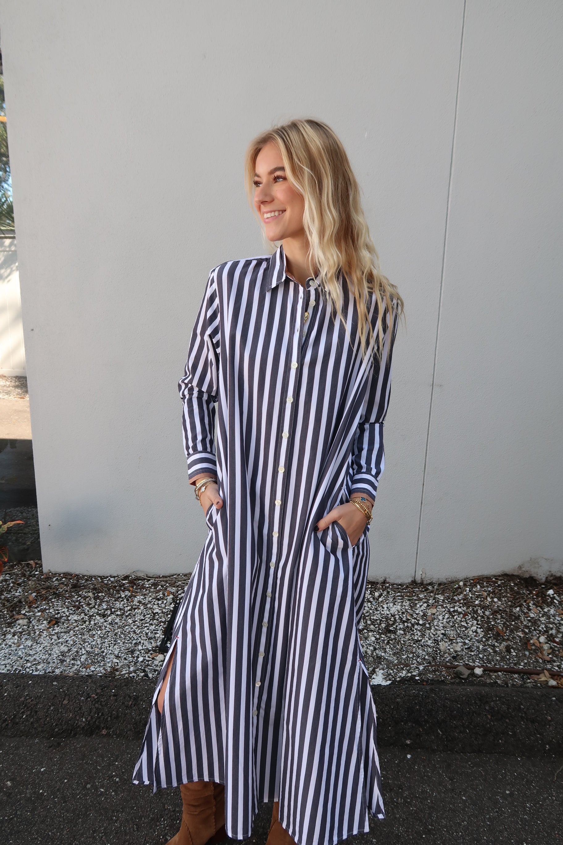 Woman wearing a grey and white striped dress standing on a sidewalk.