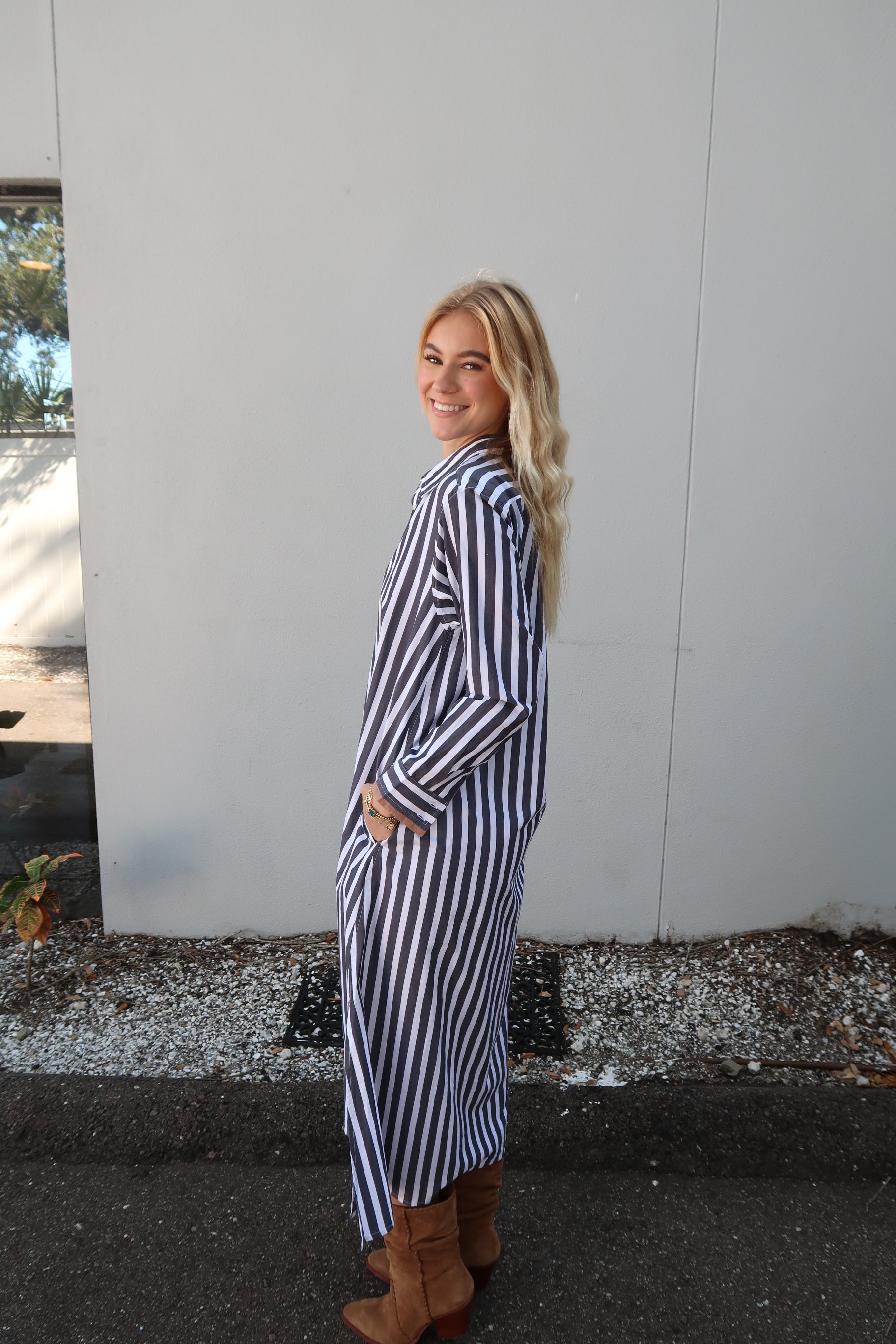 Person wearing a grey and white striped dress standing on a street. Side view