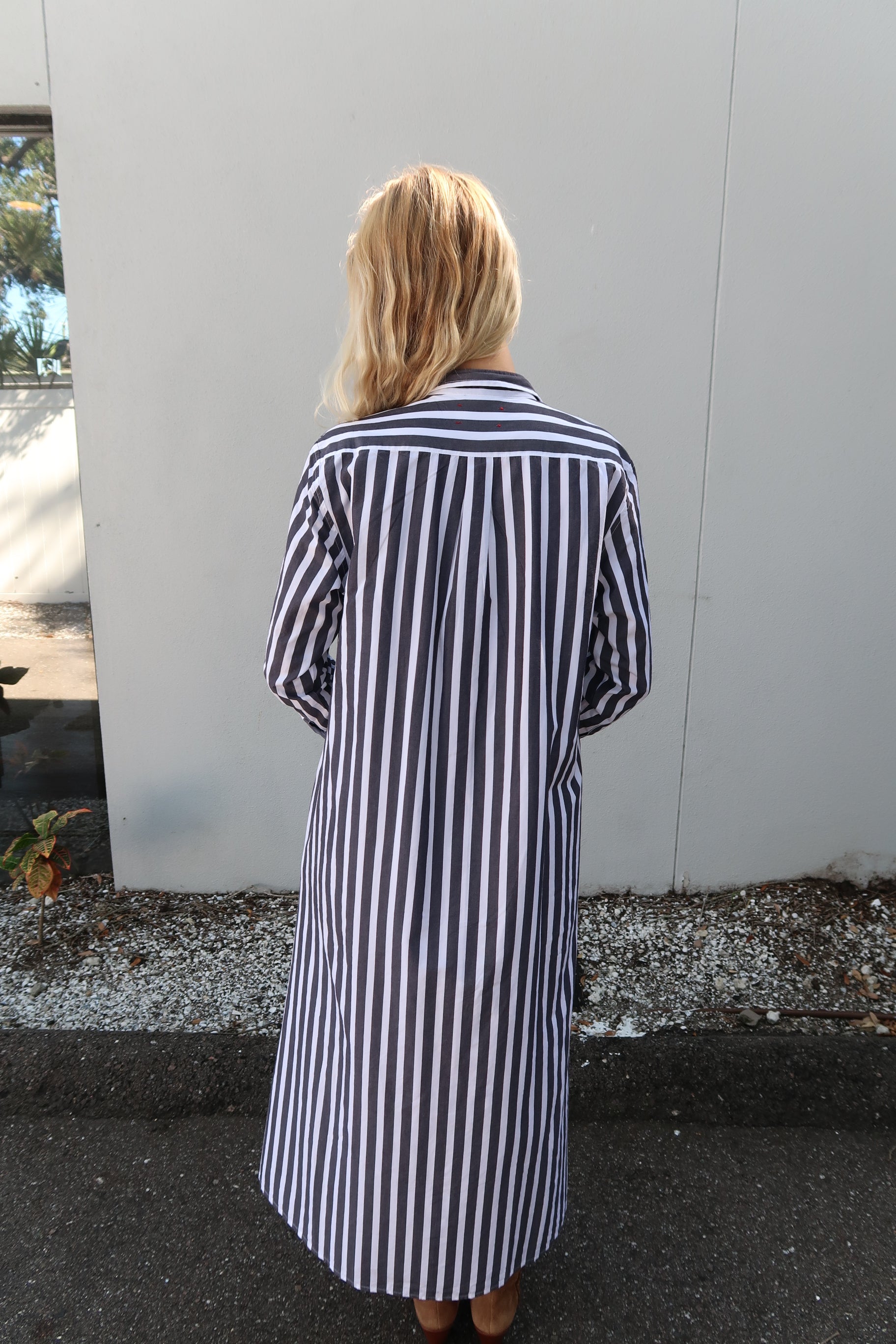 Person wearing a grey and white striped shirt standing on a sidewalk. back