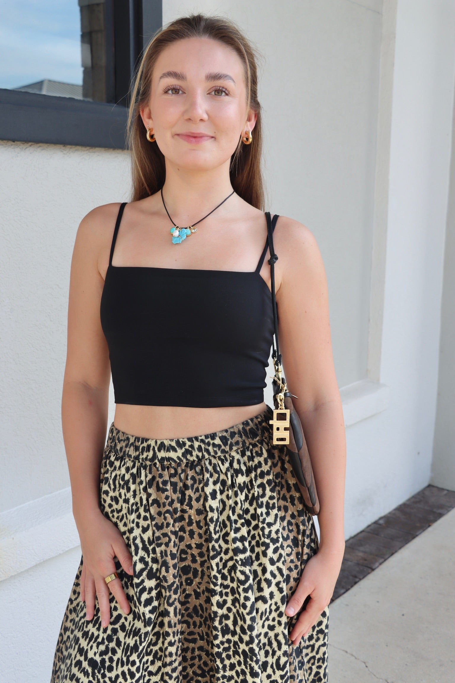 Woman wearing a black top and leopard print skirt standing outdoors.