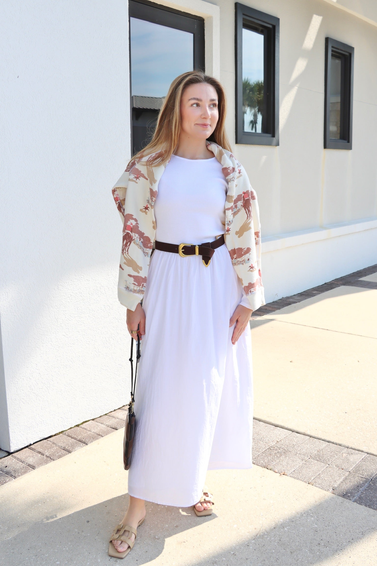 Woman in a white outfit with a floral cardigan standing in front of a white building.