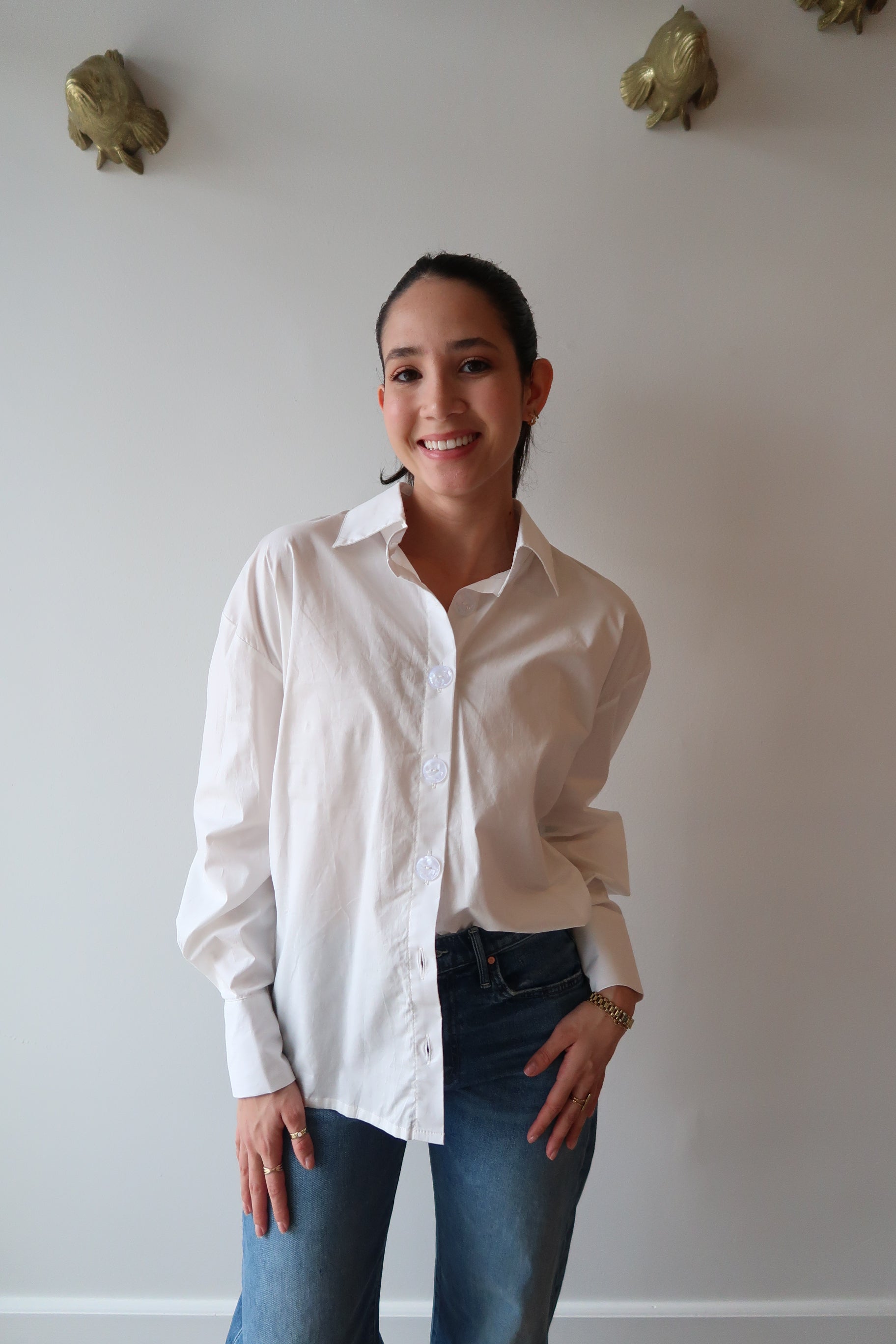 Person wearing a white shirt and blue jeans standing against a plain wall.