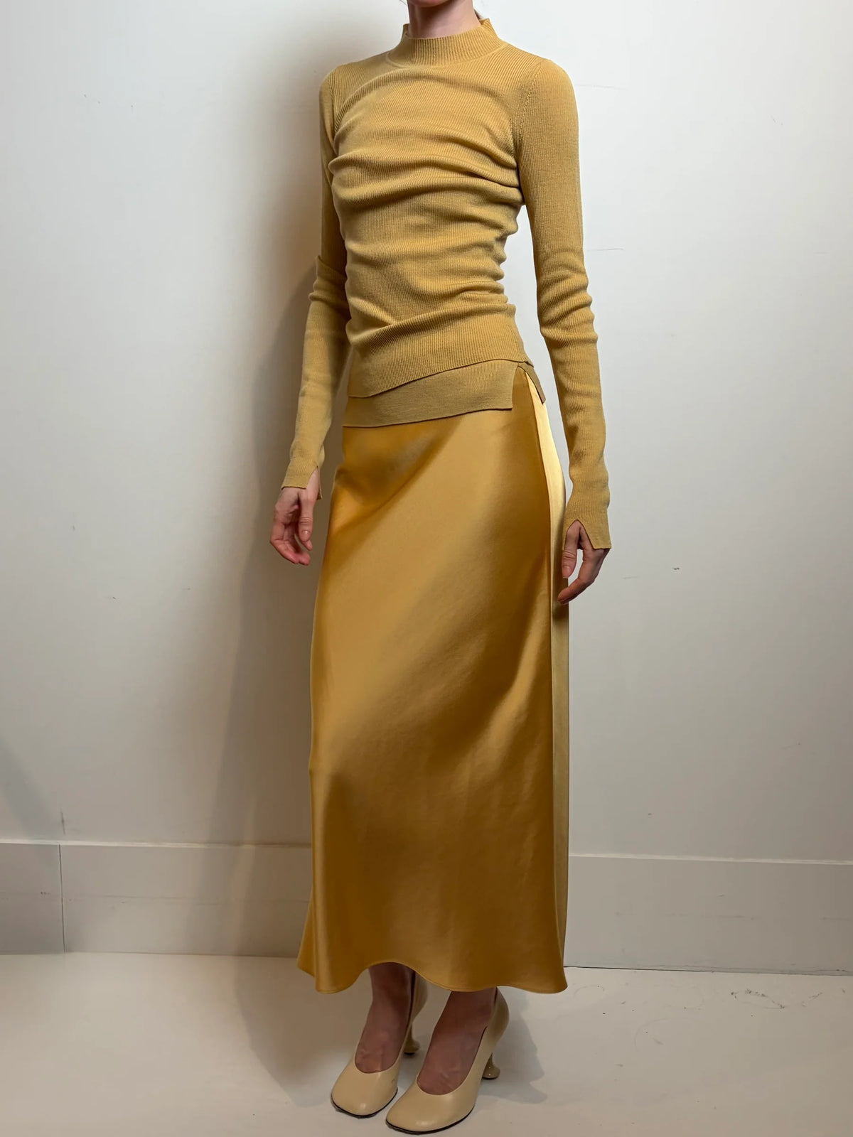 model wearing a gold skirt with a similar color long sleeve top on a white background 