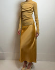 model wearing a gold skirt with a similar color long sleeve top on a white background 
