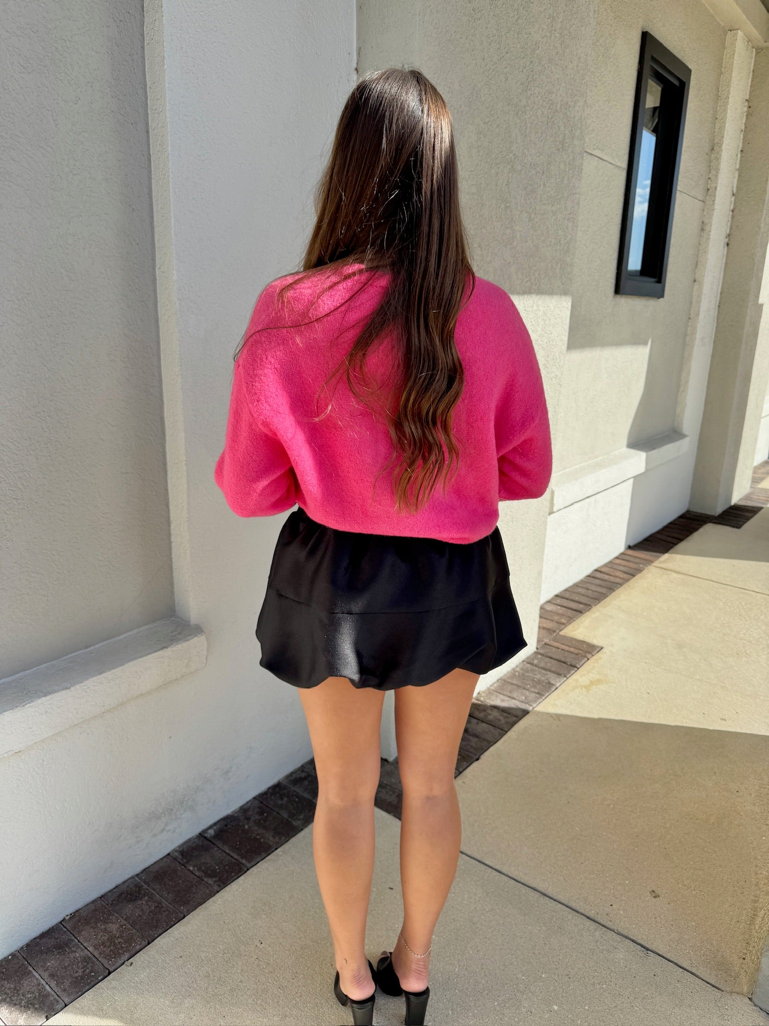 Person wearing a pink sweater and black skort standing outside a building. back view