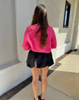 Person wearing a pink sweater and black skort standing outside a building. back view