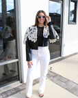 Woman wearing a black top, white pants, and a black and white lace jacket outside a building.