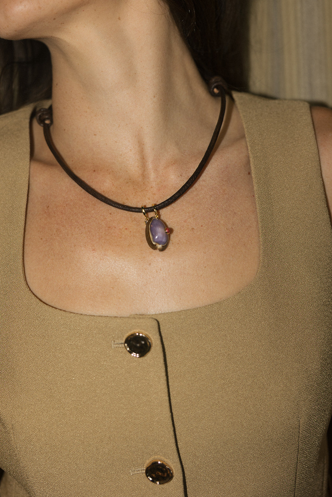 model wearing the kostas necklace with a tan top and a dim background