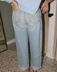 A person shown from the back wearing light-wash wide-leg denim jeans with rolled cuffs and a light blue top, standing indoors on a speckled floor.