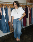 model wearing jeans and white top standing in a boutique with clothing in the background
