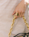 Hand holding a gold chain handbag with a snake skin pattern, against a checkered background.