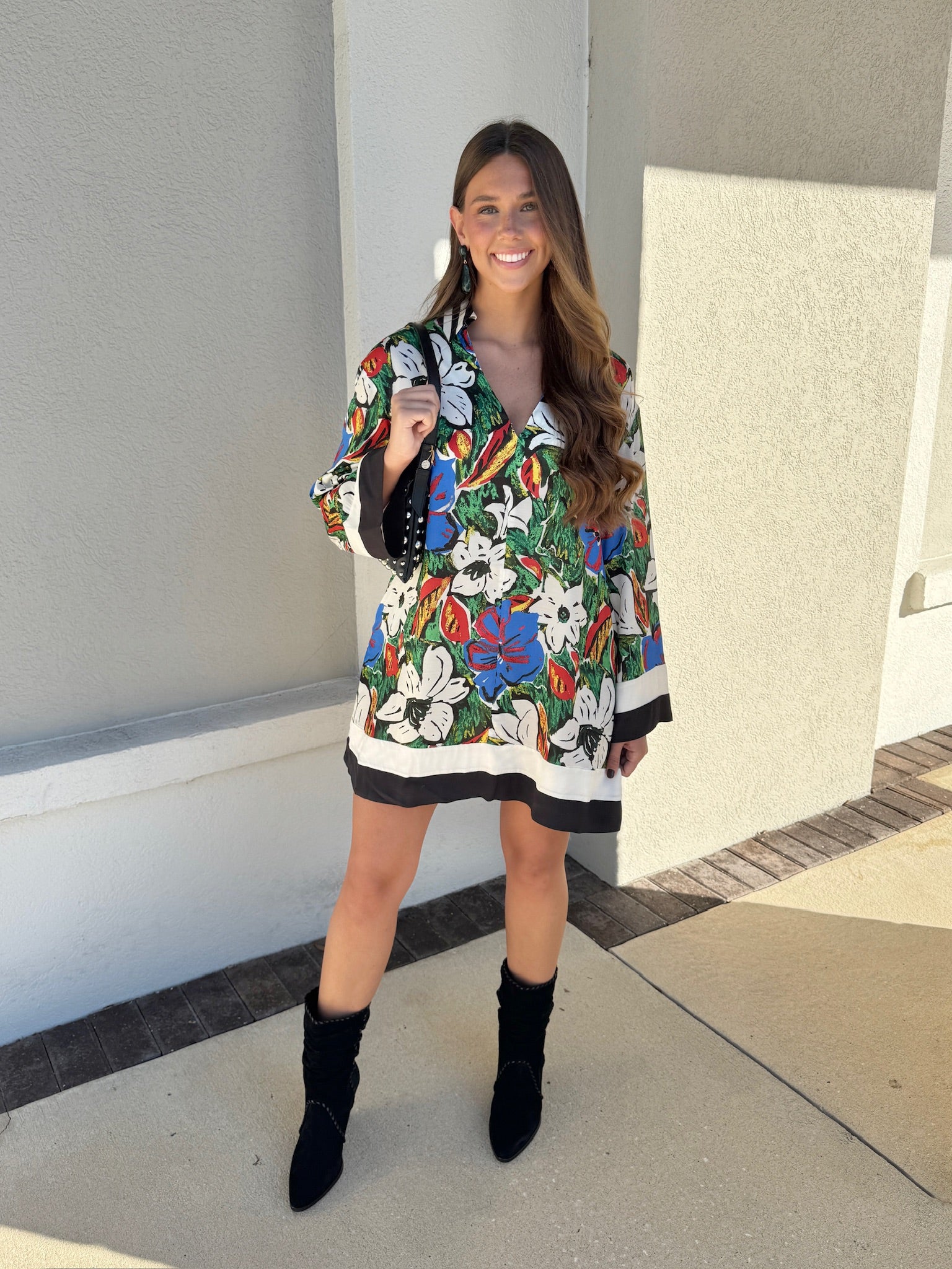 Woman wearing a colorful floral dress with black boots standing in front of a building.